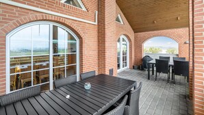 Een terras buiten met een bakstenen muur, grote ramen en een houten plafond.