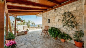 Un patio empedrado con un pérgola de madera, plantas en macetas y una silla de madera.