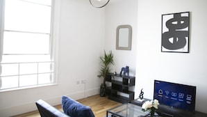 A modern living room with a large window, a black sofa, a glass coffee table, a black TV stand, and a decorative mirror.