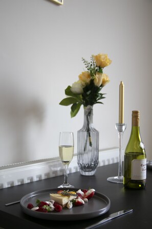 A dining table with a plate of food, a wine glass, a bottle of wine, and a vase with flowers. - Fortunae Boutique Apartment BY Fang (Sunderland)