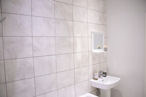 A bathroom with white tiles, a white sink, and a mirror. - Fortunae Boutique Apartment BY Fang (Sunderland)