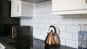 A kitchen with white cabinets, a black microwave, a copper kettle, and a glass water dispenser.