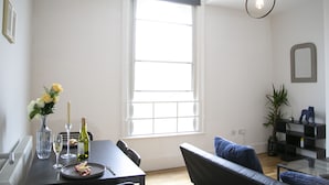 A modern living room with a dining area, a large window, a sofa, and a glass coffee table.