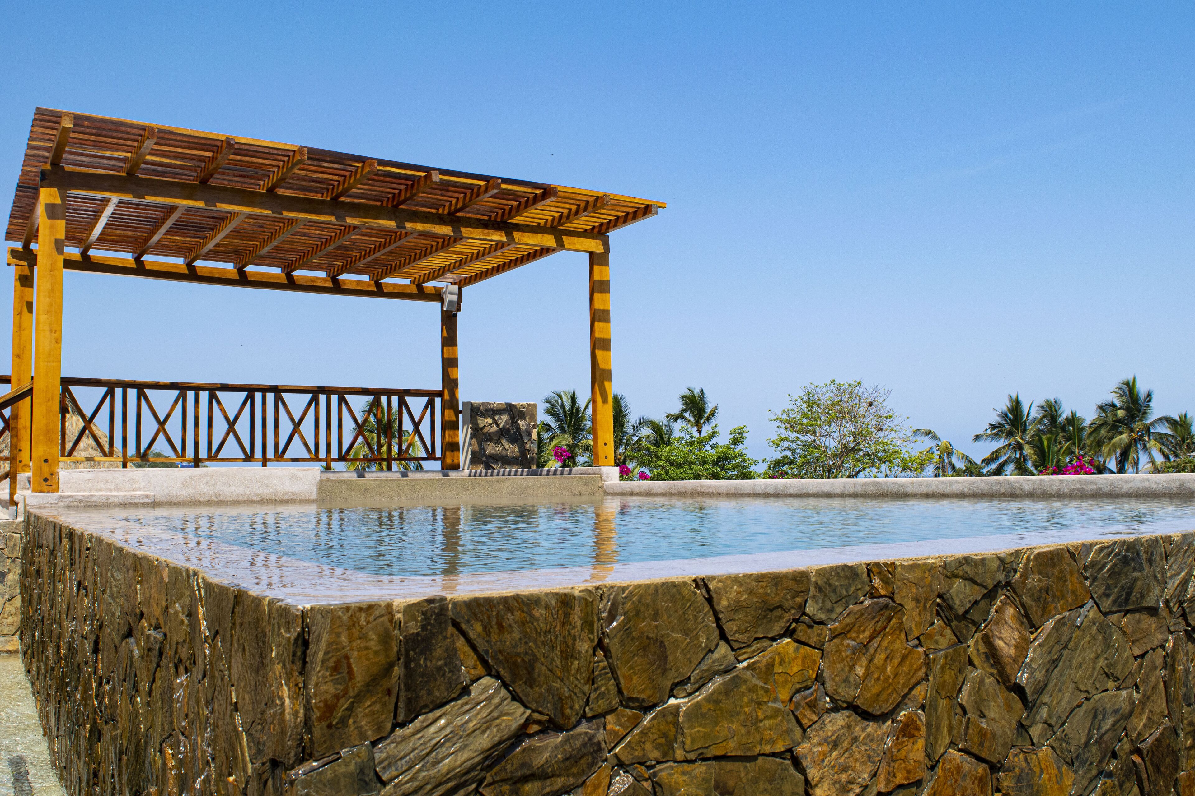 Una piscina de piedra con una estructura de pérgola de madera.