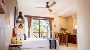Habitación de hotel con cama, ventilador de techo, zona de comedor con mesa y sillas, y vistas al exterior.