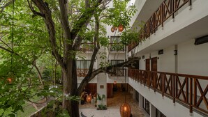 Un edificio de varios niveles con un patio central que presenta un árbol grande, bancos y faroles colgantes.