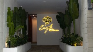 La entrada del Hotel Ciyé, con fachada de madera, un letrero de neón y plantas en macetas.