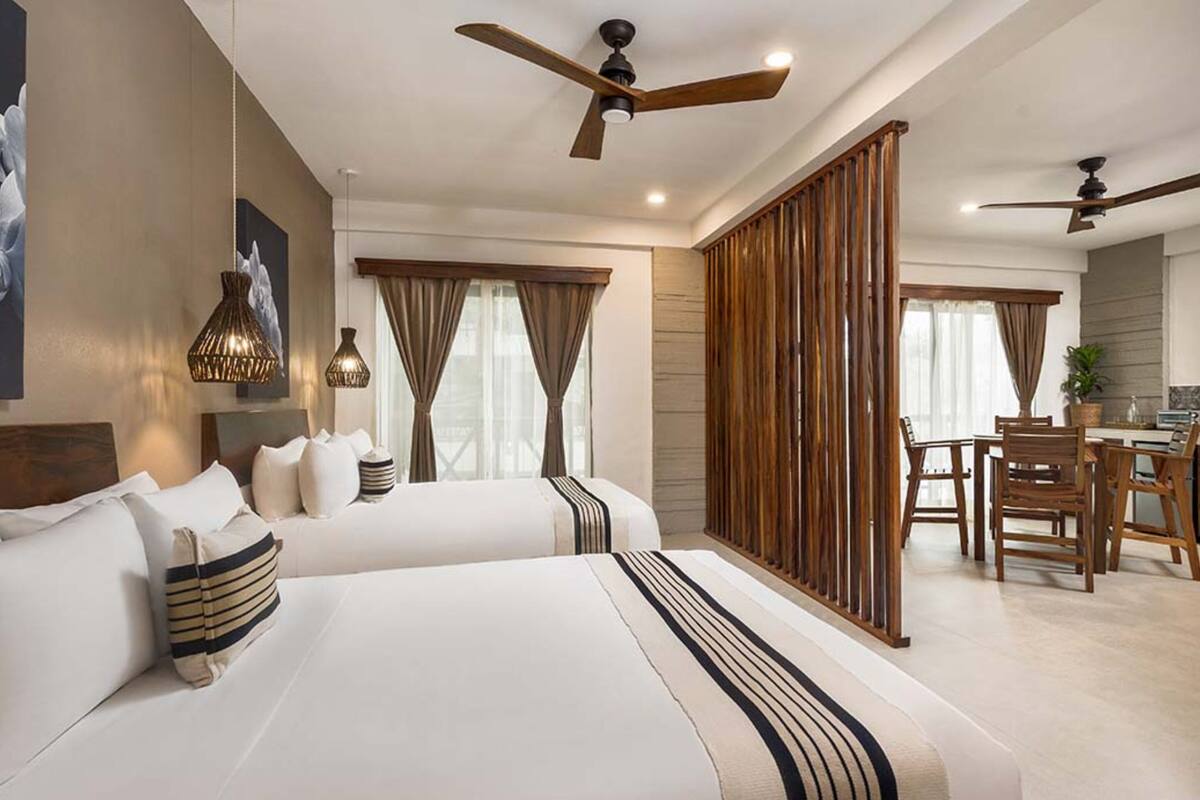 A hotel room with two beds, a dining area, and a large window with curtains.