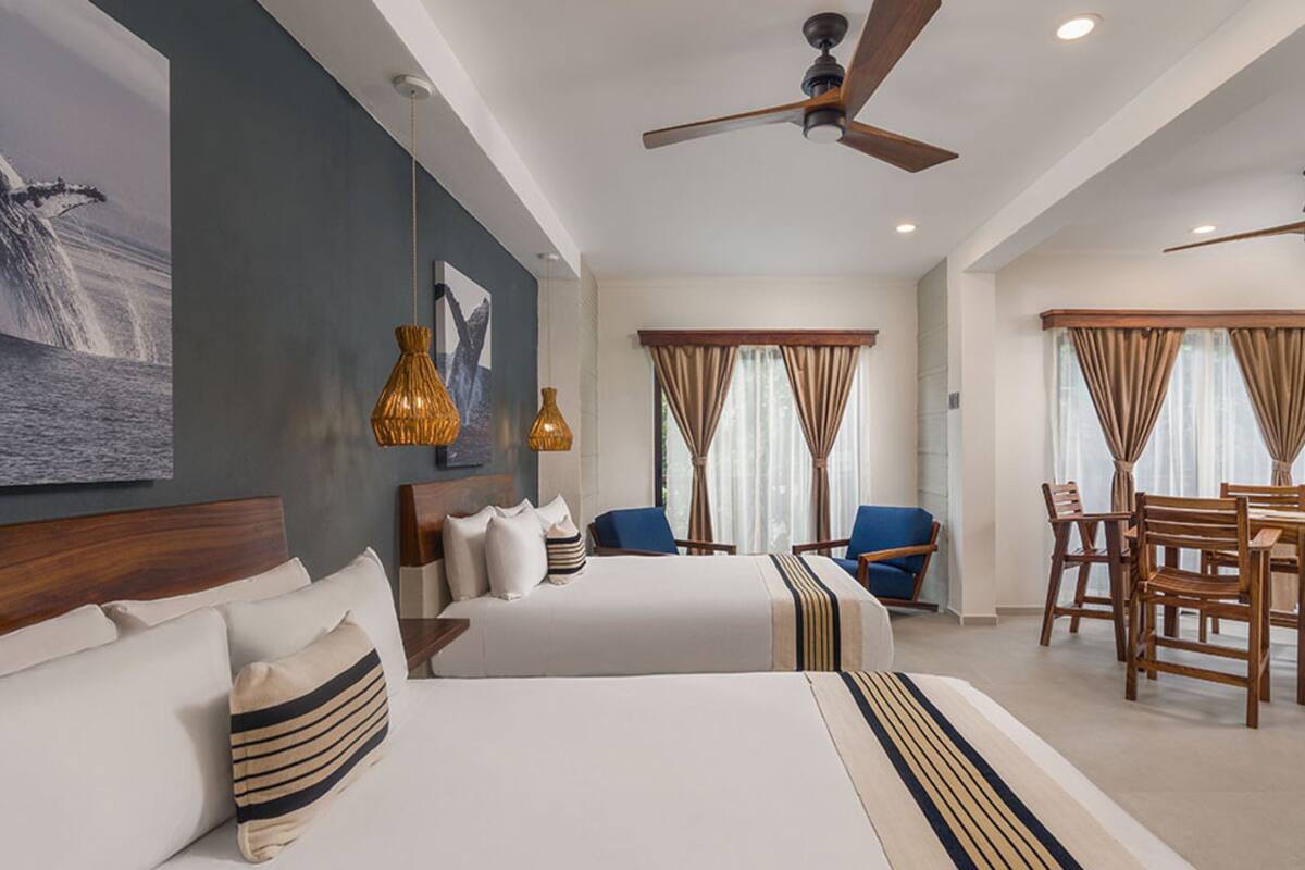 A hotel room with two beds, a dining area, and a ceiling fan.