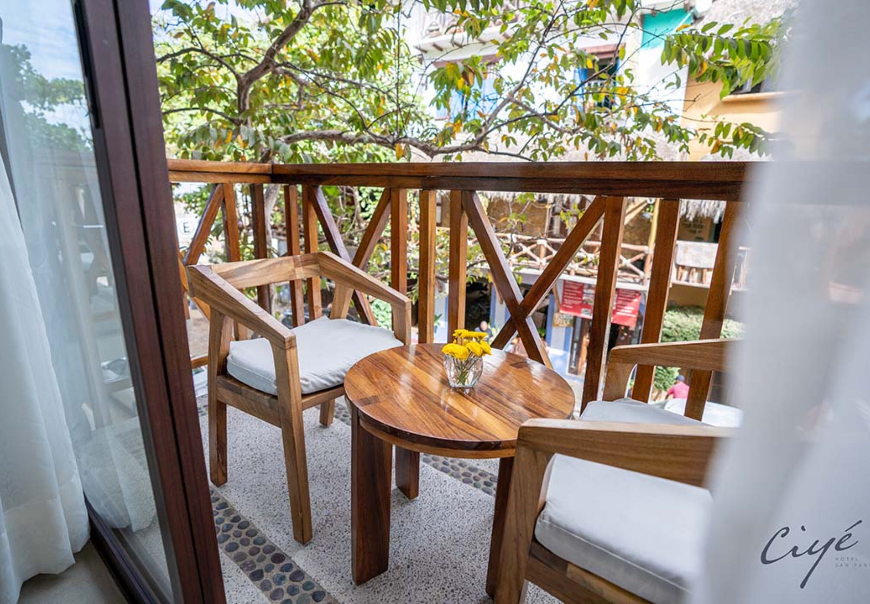 A wooden deck with chairs and a table, a glass door, and a view of trees and buildings.