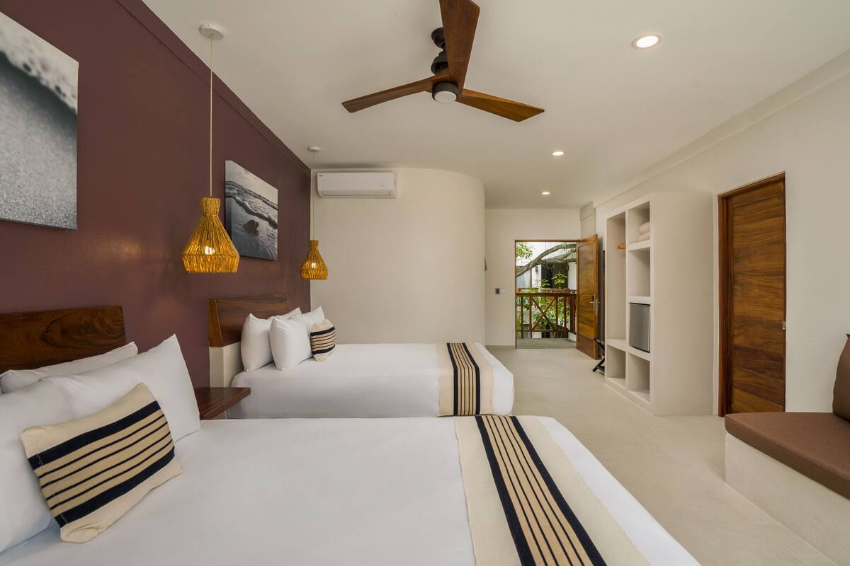 A hotel room with two beds, a ceiling fan, and a view of the outdoor balcony.