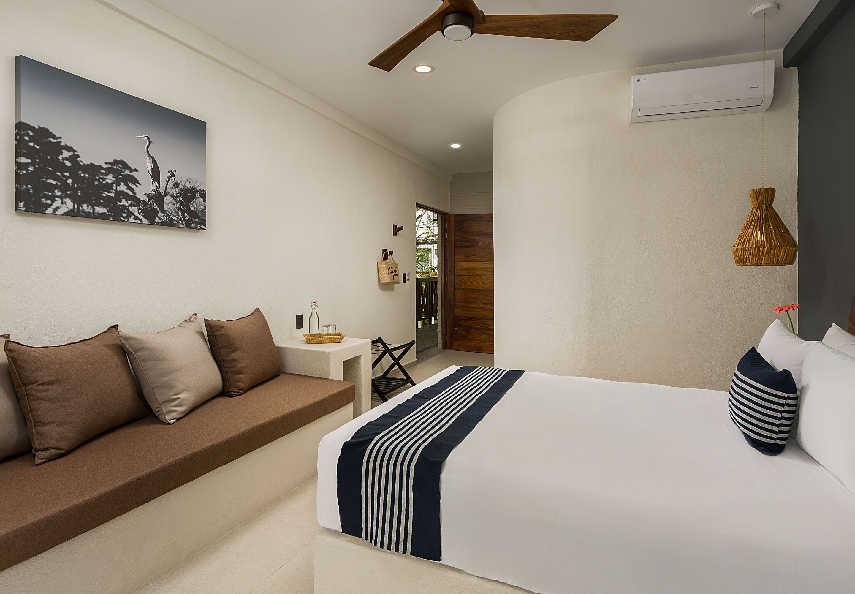 A modern bedroom with a bed, a sofa, a ceiling fan, and a wall-mounted air conditioner.