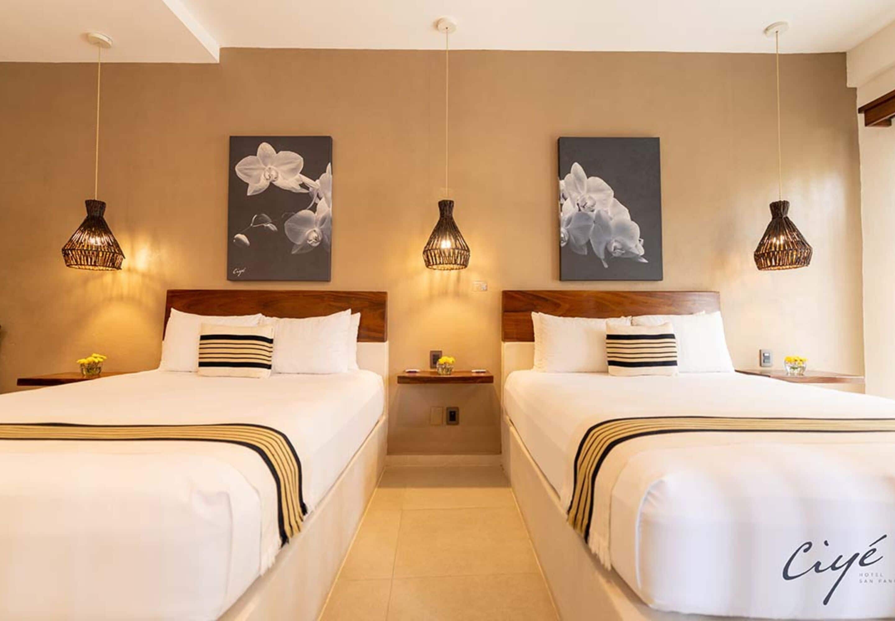 A hotel room with two beds, a wooden headboard, a small table with a vase of flowers, and artwork on the wall.