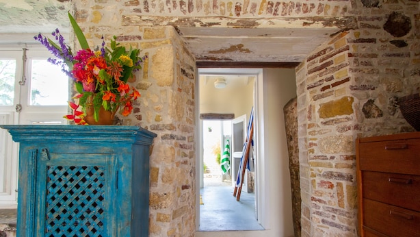 Un pasillo estrecho con paredes de piedra, un armario azul con puerta celosía y un aparador de madera.