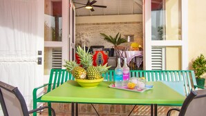 Un patio descubierto con una mesa verde, sillas, un bol de piñas, una botella de Cruzan y un vaso de agua.