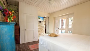 Un dormitorio con cama, cómoda, televisor y vista al exterior.