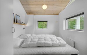 Une chambre à coucher au style minimaliste, avec un lit, deux fenêtres, un plafond en bois et un luminaire fixé au mur.