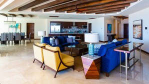 A spacious living area with a modern kitchen in the background, a dining area with a large table, and a blue sofa set. - Largest Terrace on the Ocean in Cabo! SUPER PENTHOUSE w/ 4,500 sq ft Terrace!! (Los Cabos)