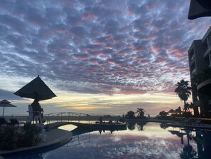 Zona de piscina en un resort con un puente, sillas de descanso y sombrillas.