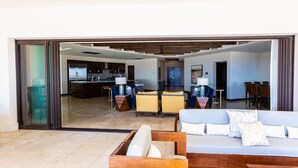 A modern living area with a sofa, a wooden coffee table, and a dining table with chairs. A kitchen is visible in the background. - Largest Terrace on the Ocean in Cabo! SUPER PENTHOUSE w/ 4,500 sq ft Terrace!! (Los Cabos)