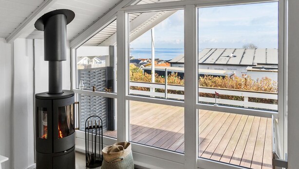En modern inredning med en vedeldad kamin, stora fönster och utsikt över ett bostadsområde.