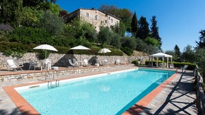 Une piscine entourée de murs de pierre et de verdure, avec des chaises longues et des parasols.