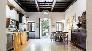 Une cuisine avec des meubles en bois, une table à manger avec des chaises, et une vue sur un jardin, visible à travers une porte en arc de cercle.