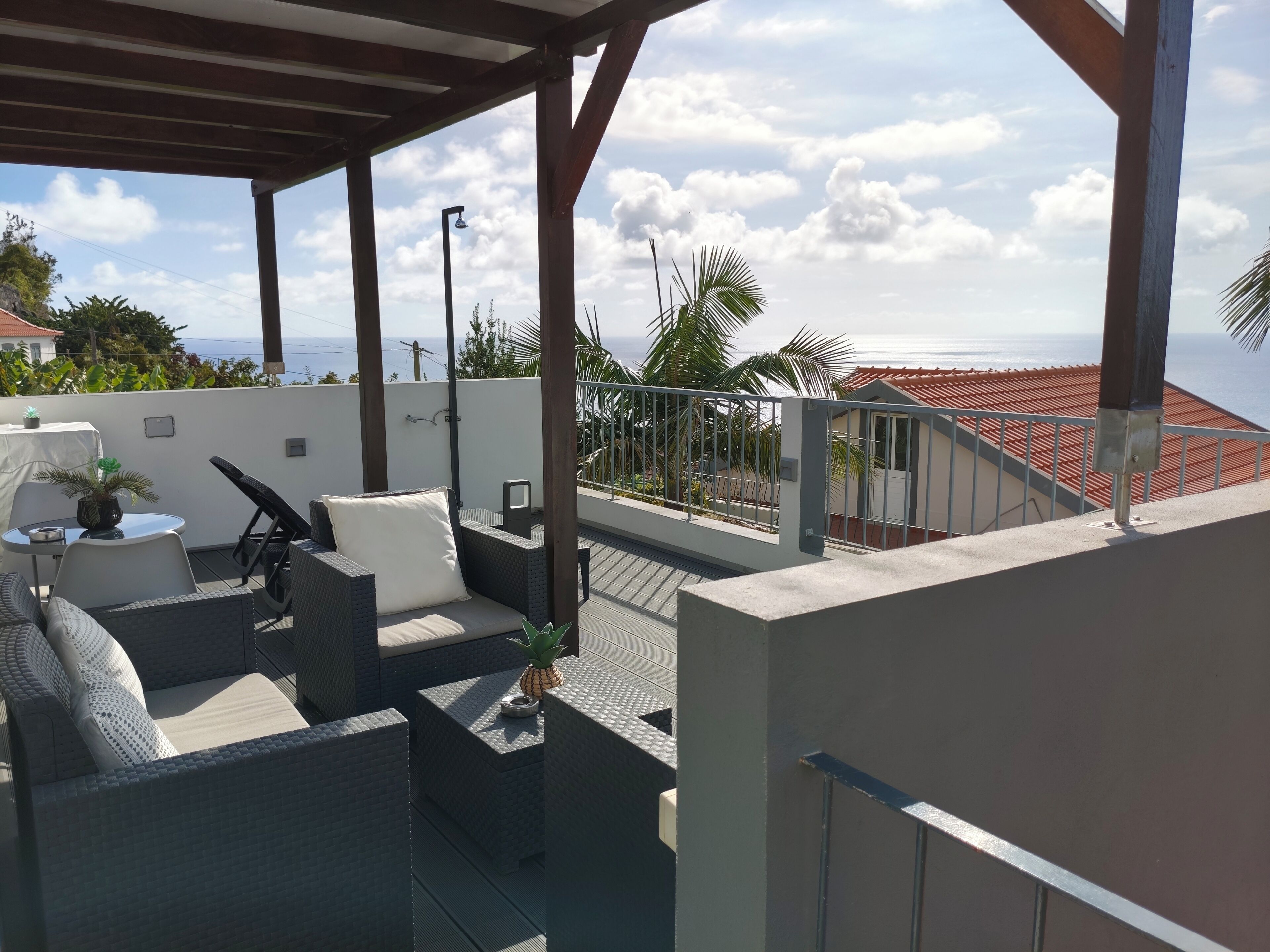 A rooftop terrace with outdoor seating, a view of the sea, and a covered area with a railing.