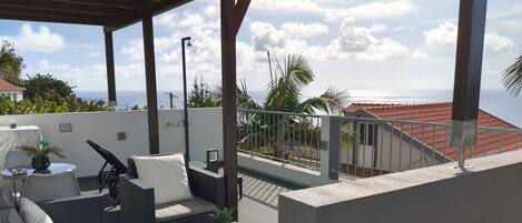A rooftop terrace with outdoor seating, a view of the sea, and a covered area with a railing.