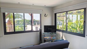 Une chambre moderne avec un grand lit, un téléviseur posé sur un meuble et un balcon offrant une vue sur la verdure et les bâtiments.