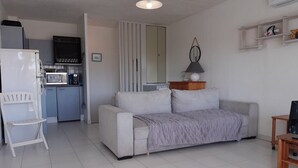 Ein kompakter Wohnraum mit Sofa, Esstisch, Stuhl, Küchenzeile und Spiegel an der Wand.