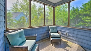 A covered porch with wicker furniture and large windows offering a view of a house and trees.