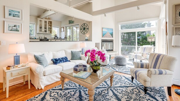 A spacious living room with a large window, a kitchen in the background, and a balcony with outdoor furniture.