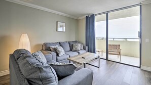 Un salón con un sofá gris, una mesa de centro de madera y vistas a un balcón con una banca.