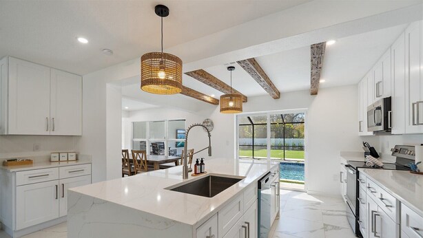 A modern kitchen with white cabinetry, a large island with a sink, and a view of a backyard with a pool.