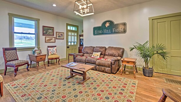 A cozy living room with a brown leather sofa, wooden chairs, a coffee table, and a patterned rug. A sign on the wall reads "Echo Hill Farm."