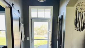 A hallway with a wooden floor, a sliding door leading to a bright outdoor area, and a hanging light fixture. - EAA Air Venture Rental 4 Bedroom, Golf-Course Home (Winneconne)