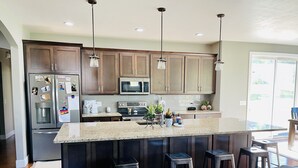 A modern kitchen with dark wood cabinets, stainless steel appliances, and a granite countertop. There are three bar stools and a large island with a sink. - EAA Air Venture Rental 4 Bedroom, Golf-Course Home (Winneconne)