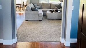 A spacious living room with a large sectional sofa, a wooden floor, and a view of the outdoors through large windows. - EAA Air Venture Rental 4 Bedroom, Golf-Course Home (Winneconne)