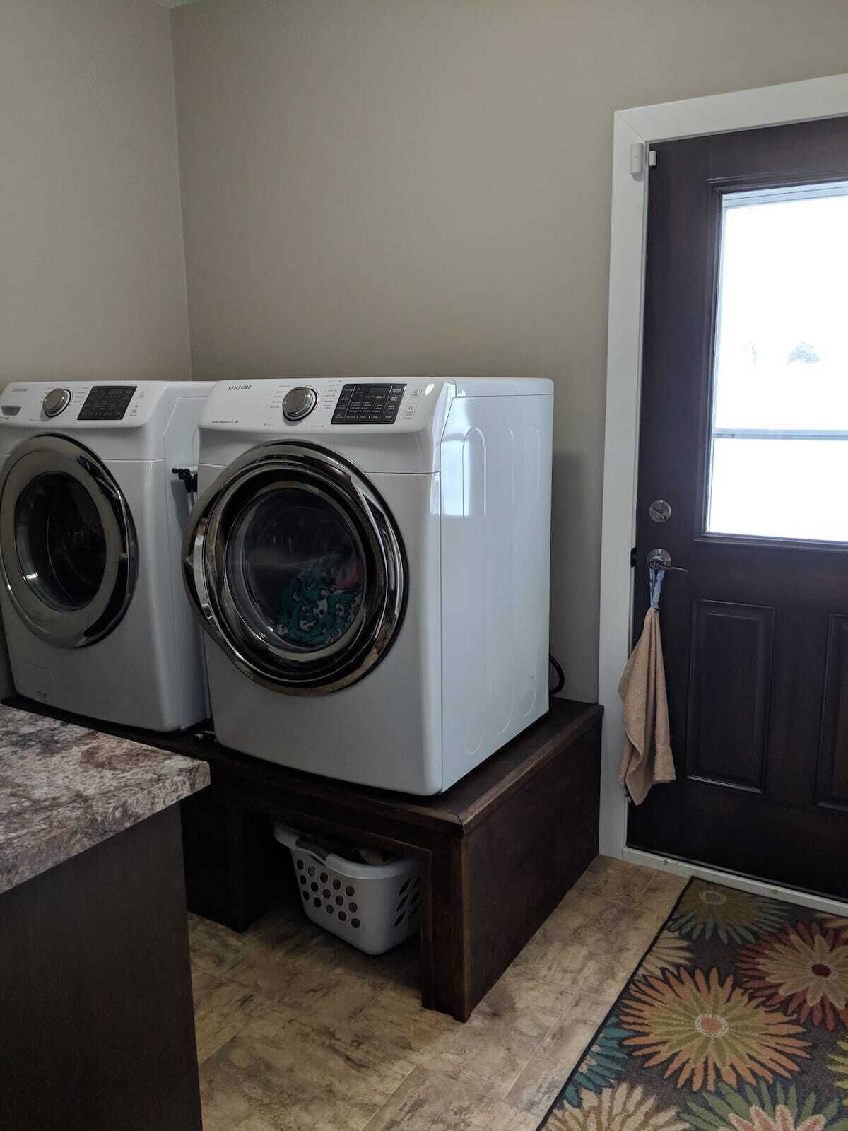 A laundry room with two front-loading washers and dryers, a dark wooden door, and a patterned rug.
