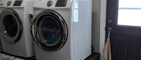 A laundry room with two front-loading washers and dryers, a dark wooden door, and a patterned rug.