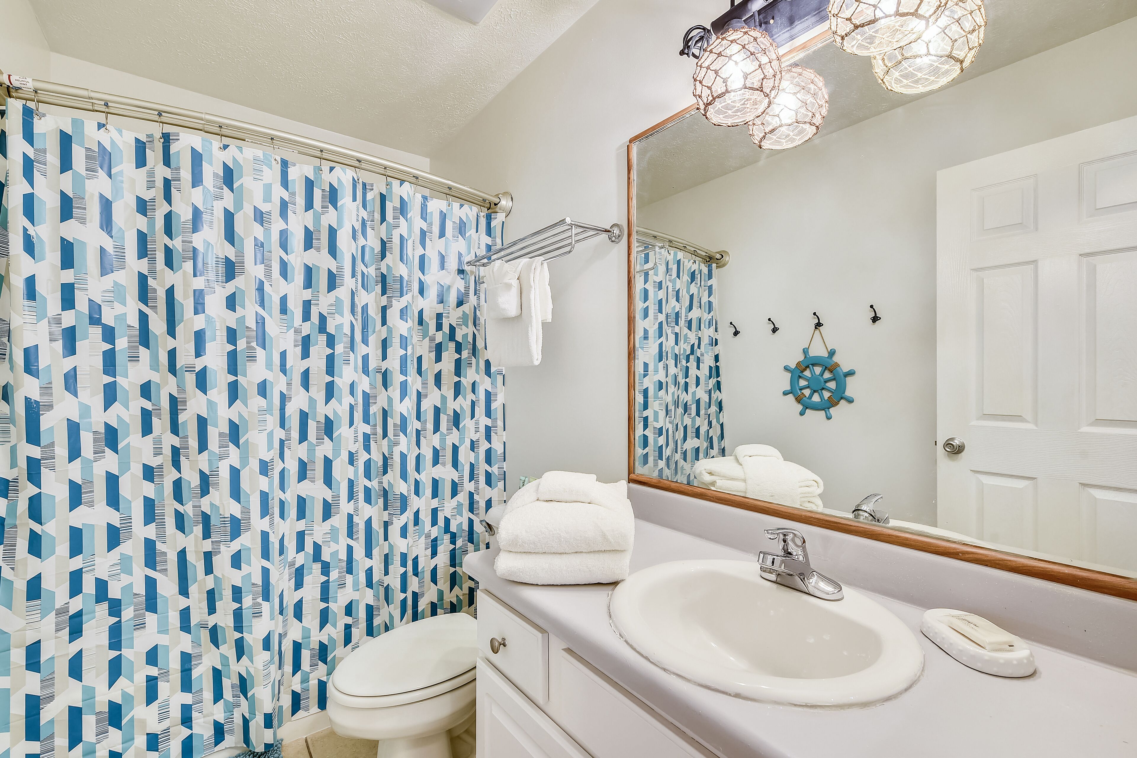 Un baño con un lavabo blanco, un espejo y una cortina de ducha con un diseño geométrico.