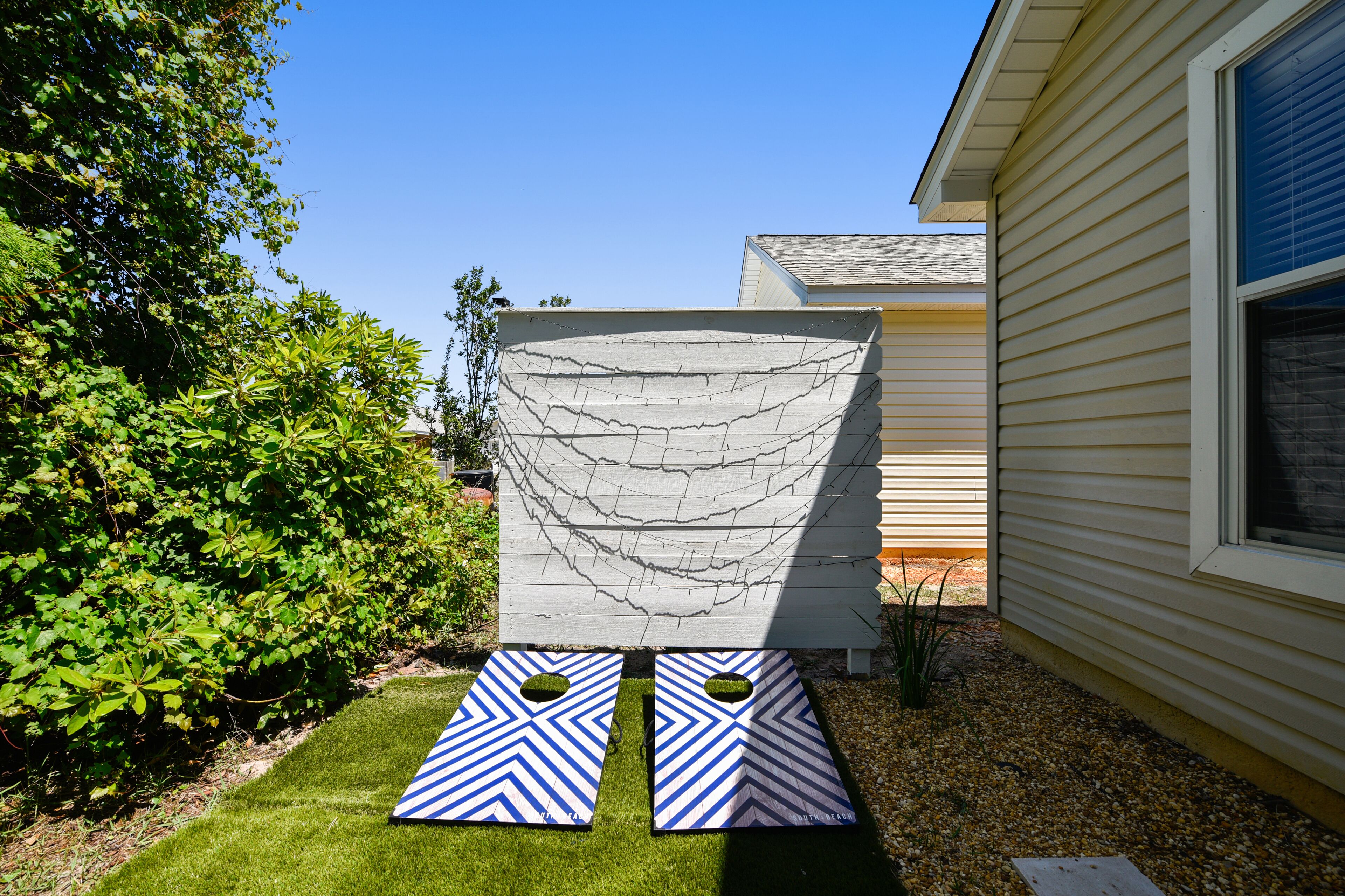 A backyard with a white fence, two blue and white chevron-patterned mats, and a house with beige siding.