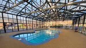 Une piscine intérieure dotée d’un toit en verre, entourée d’un sol en galets et agrémentée de sièges au bord du bassin.