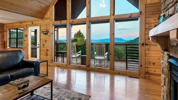 Un intérieur spacieux en bois, doté de grandes fenêtres, d’une cheminée et d’une terrasse avec des sièges d’extérieur.