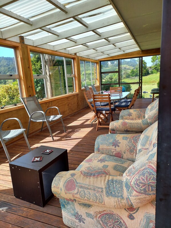 A covered outdoor seating area with wooden furniture and large windows offering scenic views.