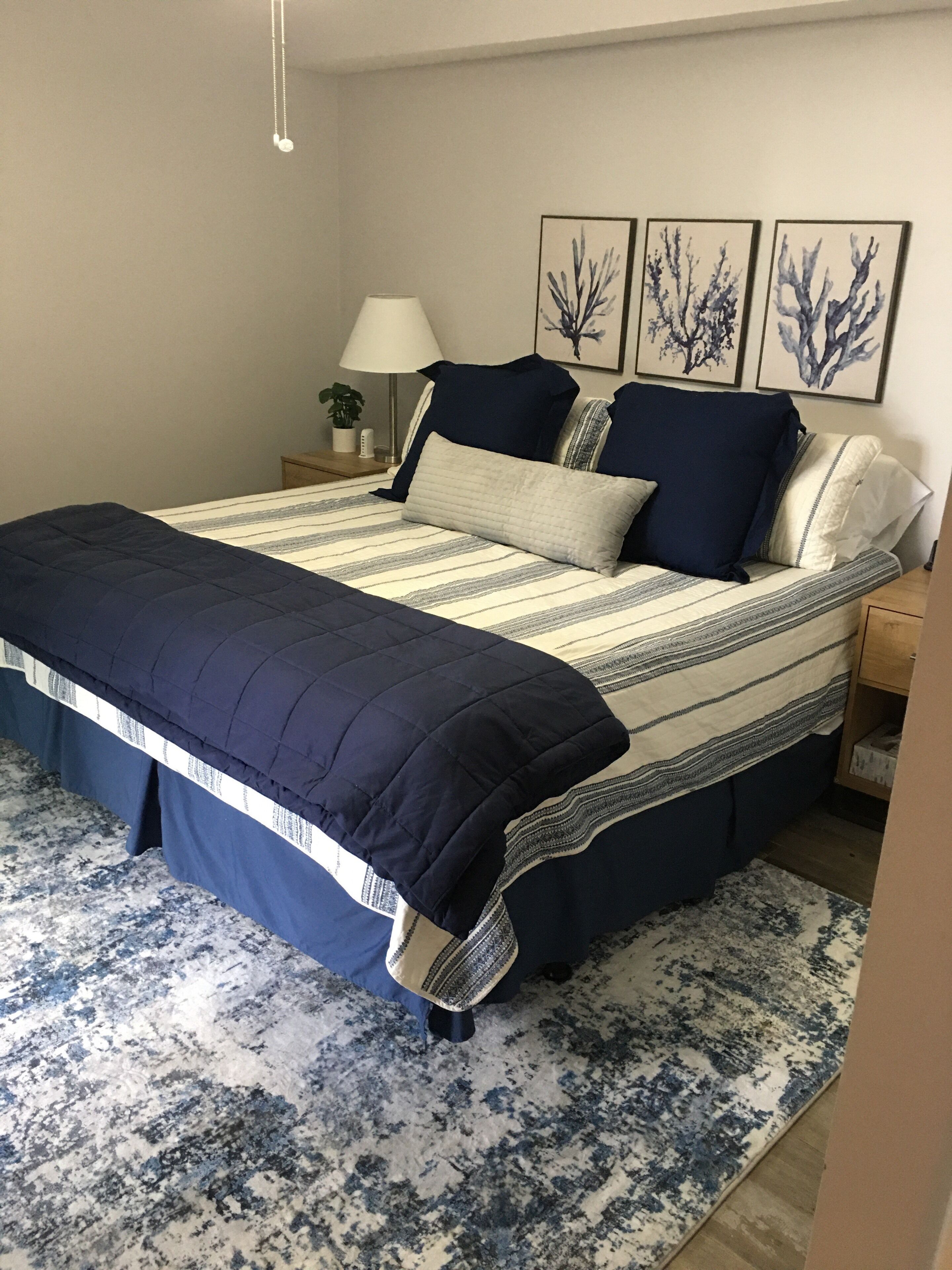 Una cama bien hecha con una colcha a rayas y almohadas a juego, una mesita de noche con una lámpara y una planta colgada en la pared.
