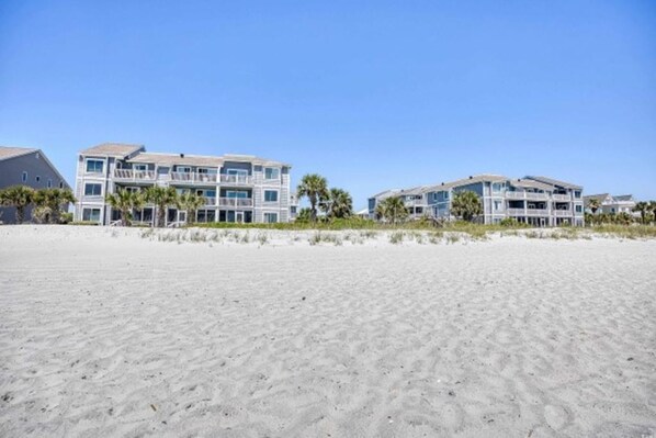 A beachfront property with multiple-story buildings, a sandy beach, and palm trees.