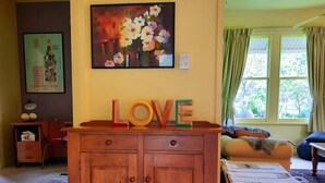 Una sala acogedora con un aparador de madera, un cuadro floral y una ventana con cortinas.