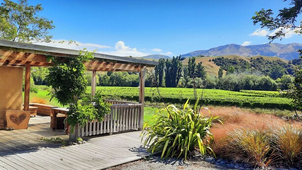 Una terraza de madera con un pérgola, mobiliario exterior y un barril de vino.